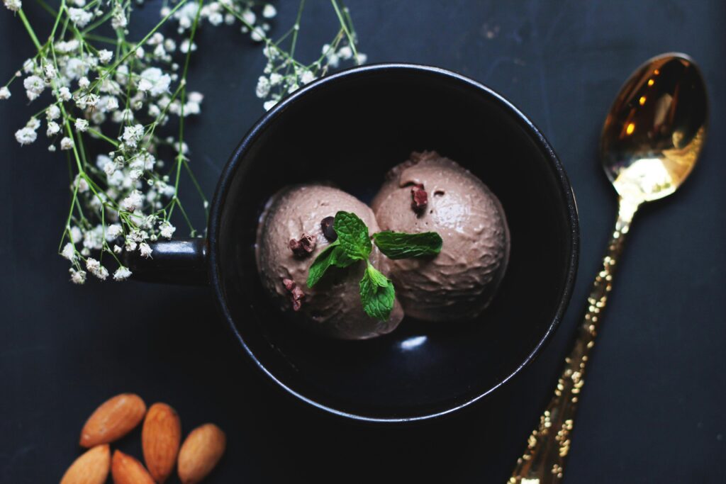 Delicious chocolate ice cream in a bowl garnished with mint leaves and almonds.